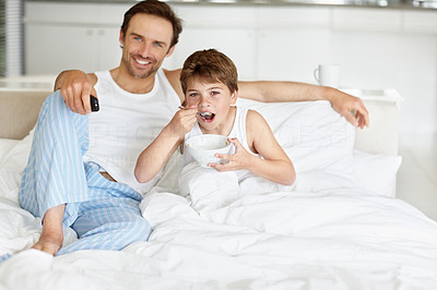 Father and son eating breakfast while watching television on bed