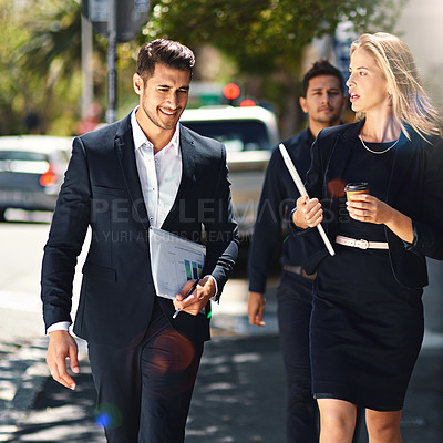 Buy stock photo Shot of corporate colleagues having a discussion while walking down the street