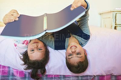 Buy stock photo Cropped shot of two young siblings reading a book together while lying upside down on a bed