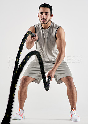 Buy stock photo Studio shot of a muscular young man exercising with battle ropes against a white background