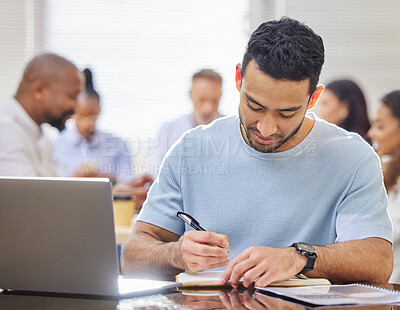 Buy stock photo Shot of a young businessman writing notes while working on a laptop in an office with his colleagues in the background