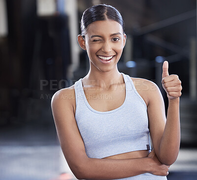 Buy stock photo Portrait of a sporty young woman winking and showing thumbs up in a gym