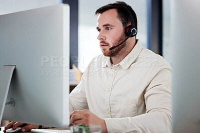 Buy stock photo Shot of a handsome young call centre agent sitting alone in his office and looking contemplative while using his computer