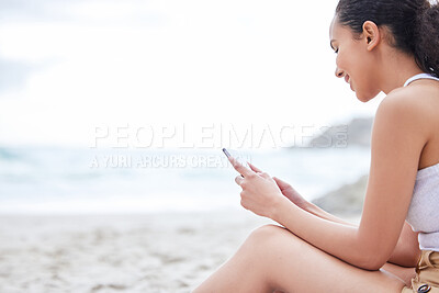 Buy stock photo Shot of a young woman using a phone at the beach