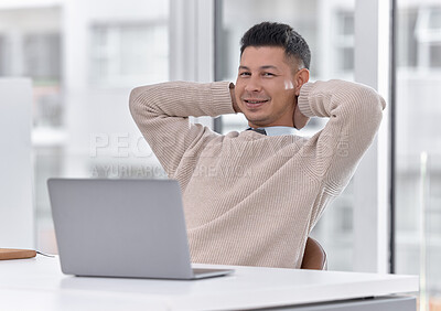 Buy stock photo Portrait of a young businessman sitting with his hands behind his head while working on a laptop in an office