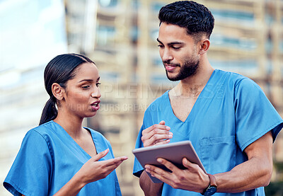 Buy stock photo Shot of two young doctors using a digital tablet in the city