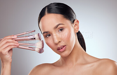 Buy stock photo Studio portrait of a beautiful young woman holding a collection of makeup brushes against a grey background