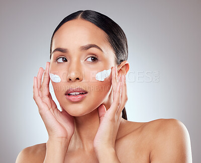 Buy stock photo Studio shot of a beautiful young woman applying moisturiser to her face against a grey background