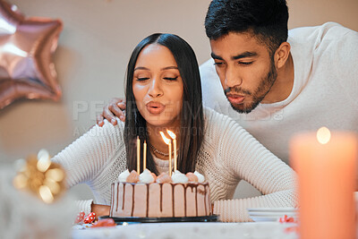 Buy stock photo Shot of a young couple blowing candles on a cake while celebrating a birthday at home