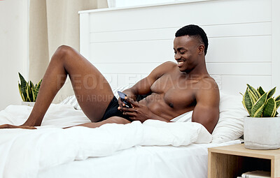 Buy stock photo Shot of a handsome young man using a cellphone while lying on his bed