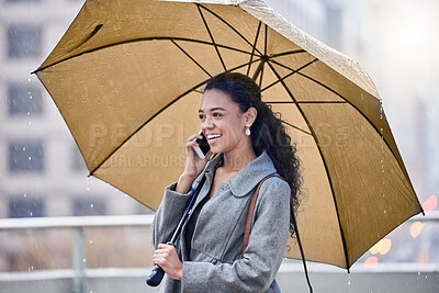 Buy stock photo Shot of a young woman holding an umbrella while on a call in the rain