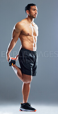 Buy stock photo Studio shot of a muscular young man stretching his legs against a grey background