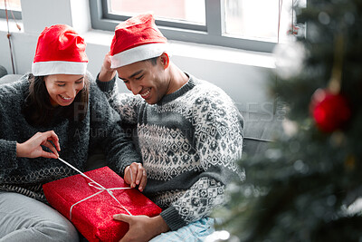 Buy stock photo Shot of a young couple unwrapping gifts on Christmas at home