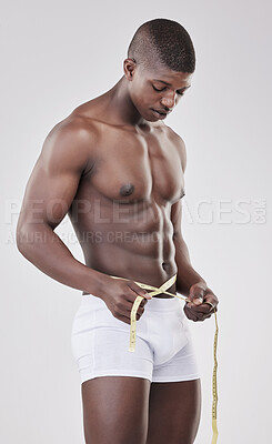 Buy stock photo Shot of a man measuring his waist using a measuring tape against a studio background