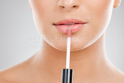 Buy stock photo Shot of a unrecognizable young woman applying lipgloss to her lips against a grey background