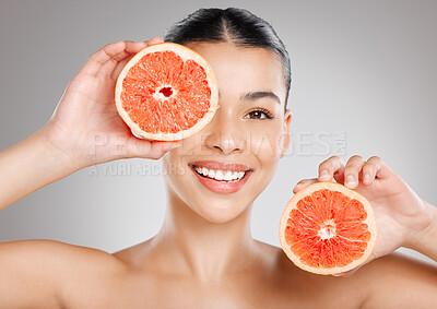Buy stock photo Studio shot of an attractive young woman holding grapefruit to her face against a grey background