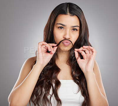 Buy stock photo Studio portrait of an attractive young woman making a moustache with her hair against a grey background