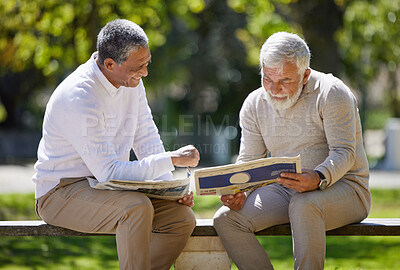 Buy stock photo Shot of two senior men sitting together on a bench in the park and reading a newspaper