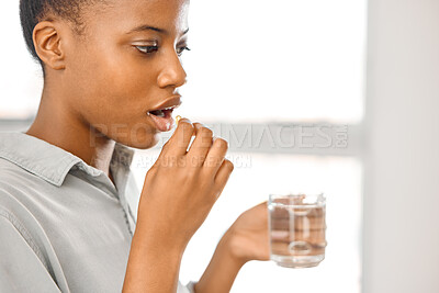 Buy stock photo Shot of a young woman taking tablets at home