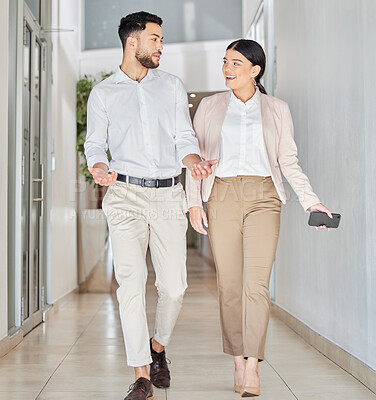 Buy stock photo Full length shot of two young businesspeople talking as they walk through a corridor in their office