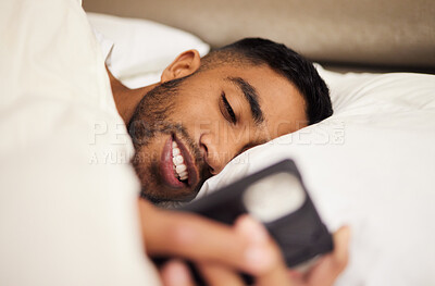 Buy stock photo Shot of a young man using his phone in bed at home