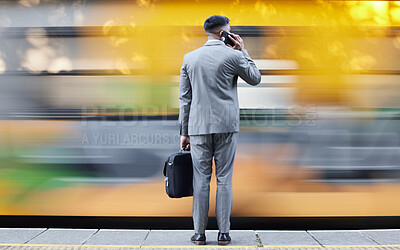 Buy stock photo Rearview shot of a young businessman talking on a cellphone while waiting for a train at a railway station during his commute