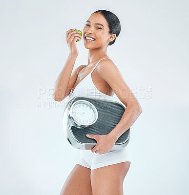 Buy stock photo Shot of an attractive young woman standing alone in the studio and posing with an apple and a scale