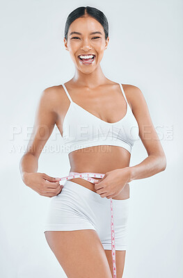 Buy stock photo Shot of an attractive young woman standing alone in the studio and using a measuring tape around her waist