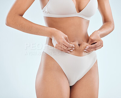Buy stock photo Cropped shot of an unrecognisable woman standing alone in the studio and pulling at fat around her belly