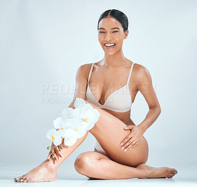Buy stock photo Full length shot of an attractive young woman sitting alone in the studio and posing while holding orchids