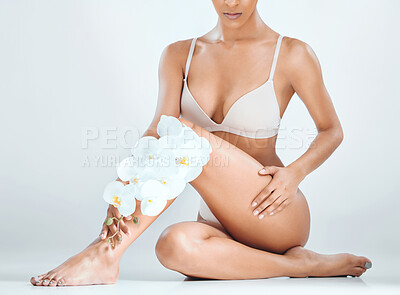 Buy stock photo Cropped shot of an unrecognisable woman sitting alone in the studio and posing while holding orchids