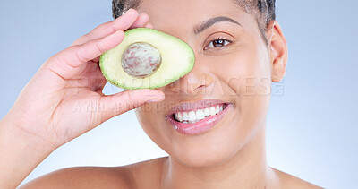 Buy stock photo Studio portrait of an attractive young woman holding a sliced avocado against a blue background
