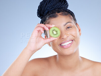 Buy stock photo Studio portrait of an attractive young woman holding a sliced kiwi against a blue background