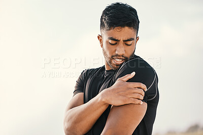 Buy stock photo Cropped shot of a handsome young male athlete holding his shoulder in pain while exercising on the beach
