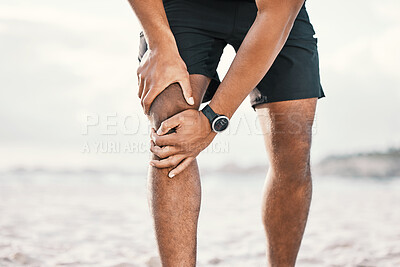 Buy stock photo Cropped shot of an unrecognizable male athlete holding his knee in pain while exercising on the beach