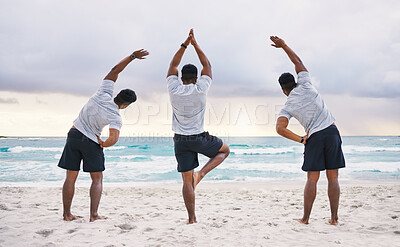 Buy stock photo Rearview shot of three unrecognizable male athletes practicing yoga on the beach