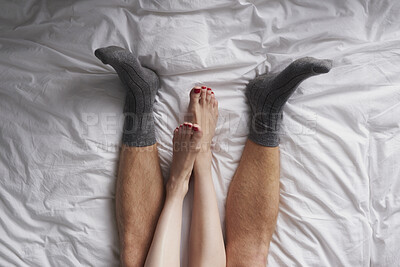 Buy stock photo Closeup of the legs of a couple lying in bed affectionately cuddling