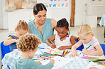 Beautiful mixed race woman crouching down to watch a group of diverse children colour in preschool. Small and cute kids sitting together and drawing on paper while their Hispanic teacher helps them