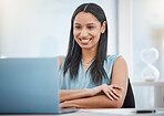 Happy young mixed race businesswoman smiling while enjoying working on a laptop sitting in a chair in an office at work. One hispanic female boss sending an email using a laptop at a desk at work. Feeling Satisfied