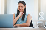 Happy young mixed race businesswoman smiling while enjoying working on a laptop sitting in a chair in an office at work. One hispanic female boss sending an email using a laptop at a desk at work