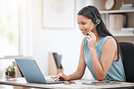 Young happy hispanic female call center agent working on a laptop and answering calls while sitting in a chair in an office alone at work. One hispanic businesswoman typing emails and smiling at work