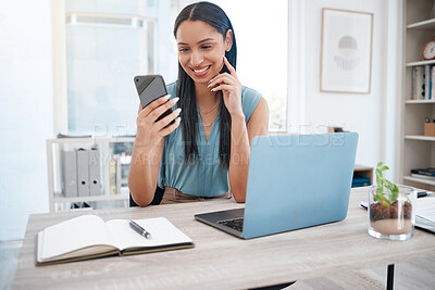 Buy stock photo Smiling mixed race businesswoman using smartphone and working on a laptop at her desk. One confident female entrepreneur using social media or browsing the internet while sitting in her office