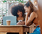 Two happy and cheerful mixed race friends using social media on a phone while sitting together at a table at a cafe. Positive hispanic females laughing while looking at a phone at a restaurant