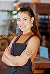 Portrait of one smiling beautiful asian business owner standing with her arms crossed in her cafe. Confident and successful mixed race woman wearing an apron in her restaurant. Ambitious entrepreneur