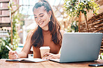 Freelance entrepreneur working in a restaurant, planning, writing notes in her notebook. Smiling young businesswoman drinking coffee, working on her laptop in a cafe. Teleworking businesswoman in cafe