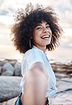 A young mixed race woman smiling on the beach while reaching out her hand. Happy hispanic female with a cool afro hairstyle outdoors