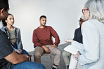 Closeup of a young diverse support group during a meeting with a professional female therapist. Group of employees looking serious during a team counselling session. Mental health in the workplace
