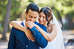 Happy young romantic couple on their wedding day. Groom kissing his brides hand while she embraces him from behind. Newlywed couple with nature background