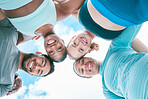 Portrait of a diverse group of happy sporty people from below joining their heads together in a huddle for support and unity with cloudy sky in the background. Cheerful motivated athletes ready for exercise workout outside