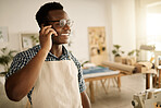 Smiling designer making a phone call in his studio. Fashion designer talking during a cellphone call. Small business owner using his smartphone. African American tailor making a phone call